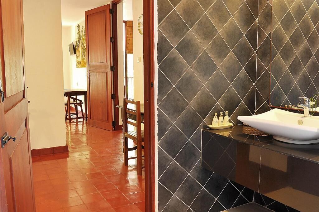 A bathroom with a dark tiled wall, a white sink, and a wooden door.