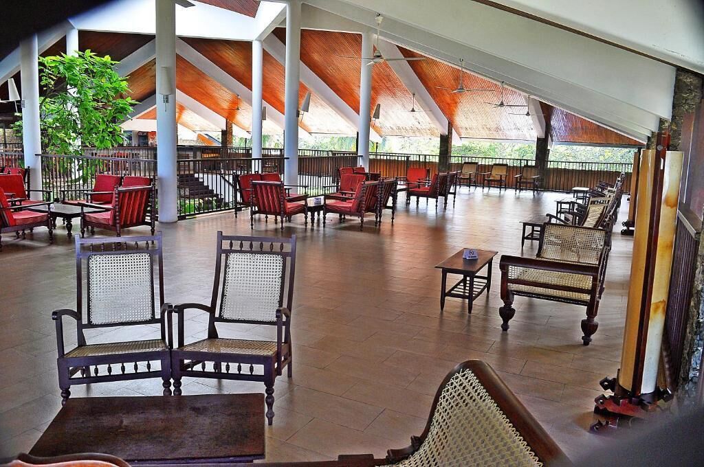 A covered outdoor seating area with wooden tables and chairs, surrounded by a low fence.