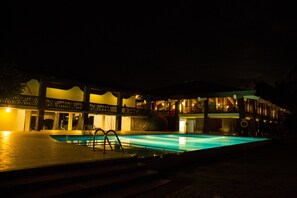 A swimming pool with a wooden deck and a building with multiple balconies in the background.