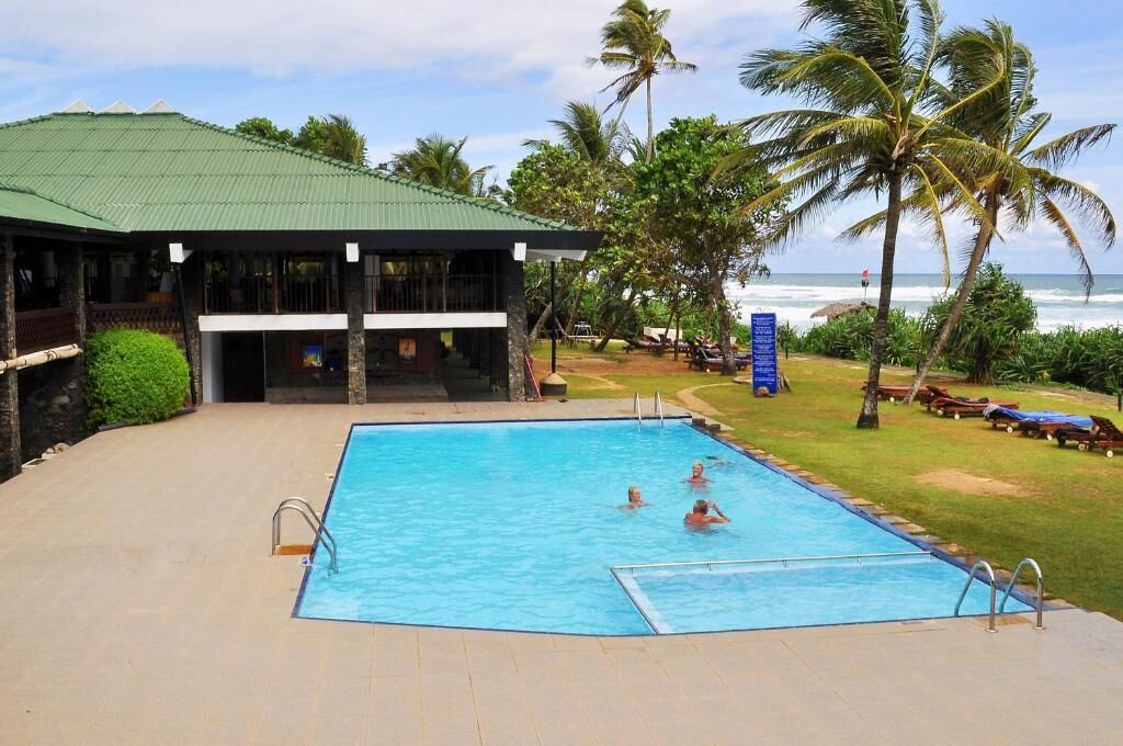 A swimming pool with a covered area, palm trees, and a view of the ocean.