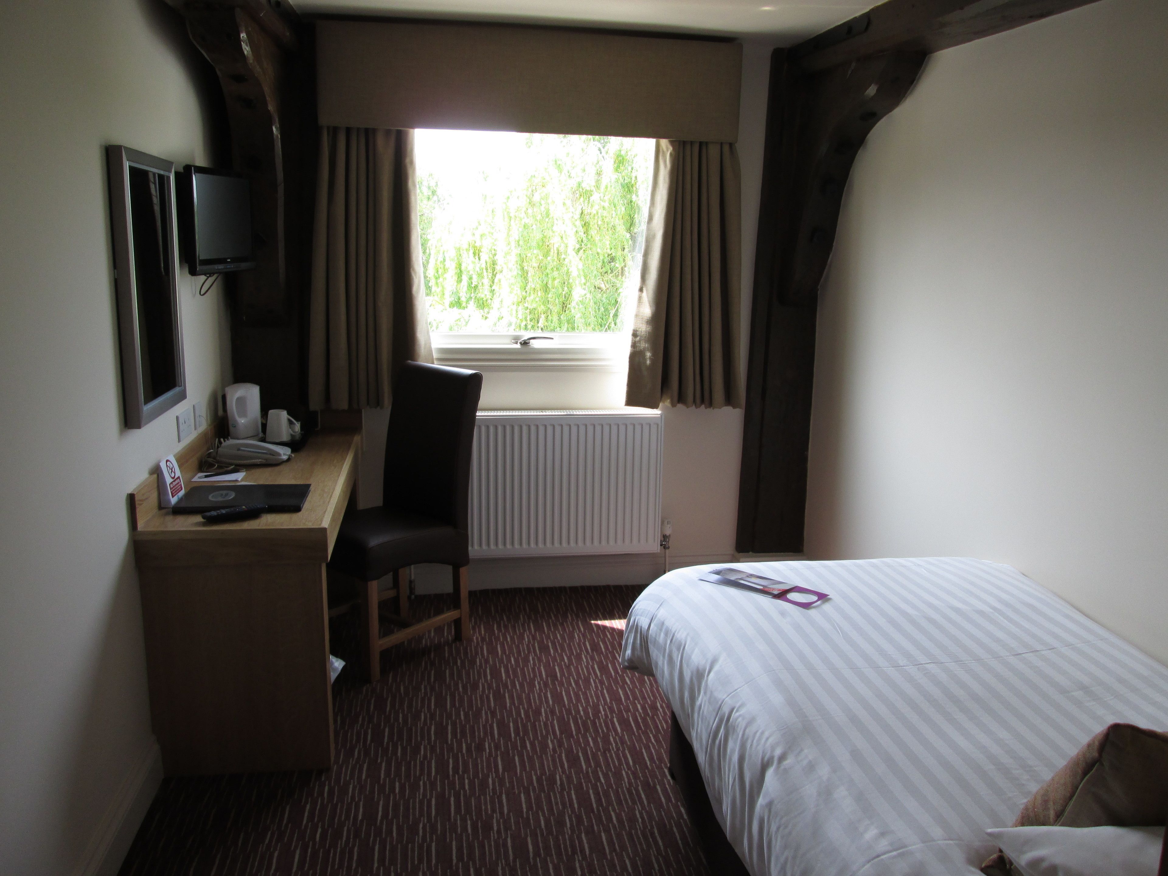 A hotel room with a bed, a desk with a chair, a television, and a window with curtains.