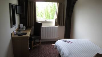 A hotel room with a bed, a desk with a chair, a television, and a window with curtains.