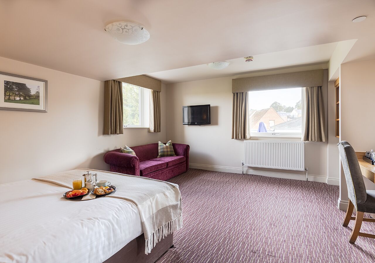 Une chambre d’hôtel comprenant un lit, un canapé, une télévision et une table à manger où le petit-déjeuner est servi.