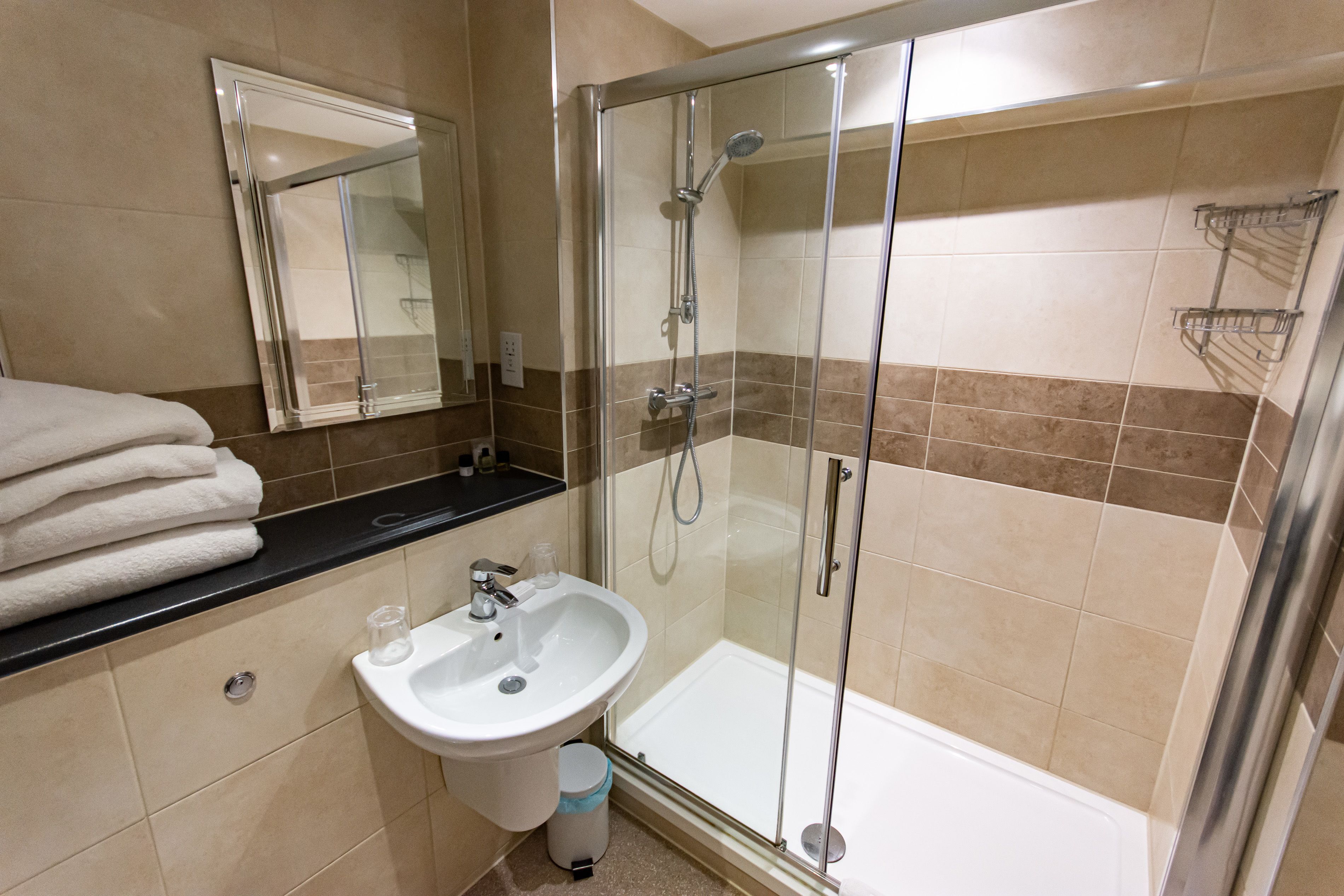 Een badkamer met een douche met glazen wand, een wastafel en een spiegel.