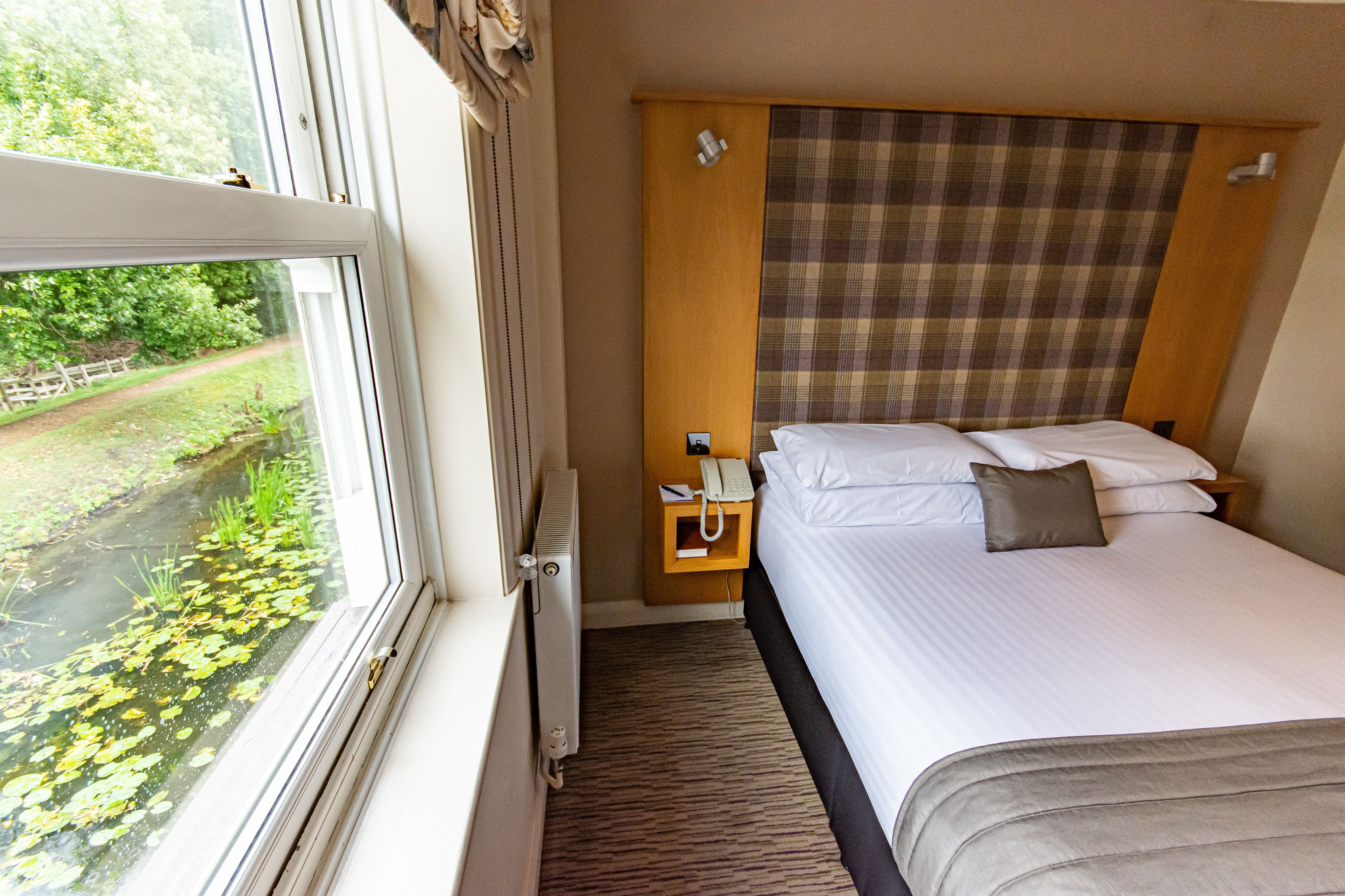 Une chambre d’hôtel avec un lit, une table de chevet, un téléphone et une fenêtre donnant sur un paysage verdoyant.