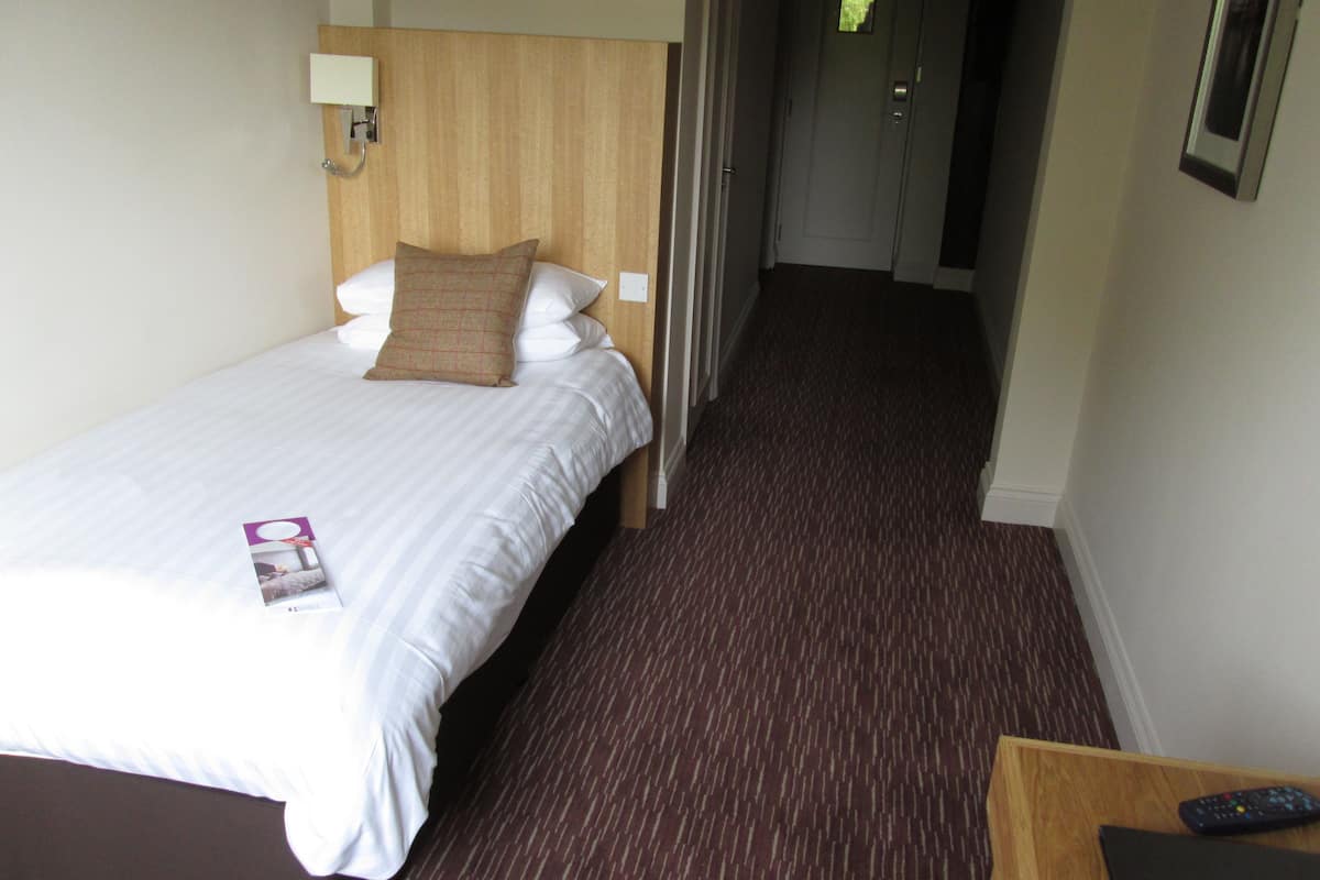 Une chambre d’hôtel avec un lit, une table de chevet, une télécommande et une porte donnant sur une autre pièce.