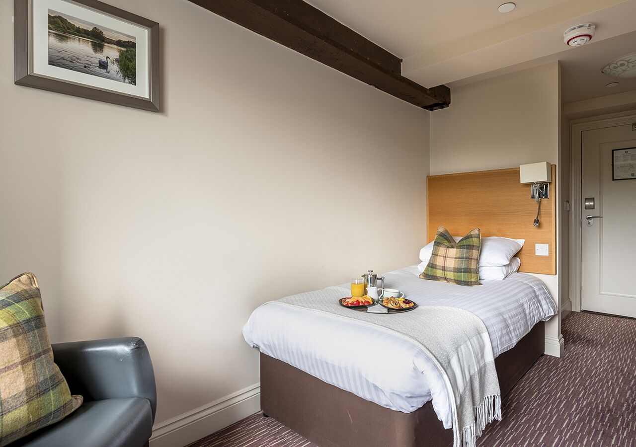 Quarto de hotel com uma cama, uma cadeira e um tabuleiro de pequeno-almoço sobre a cama.
