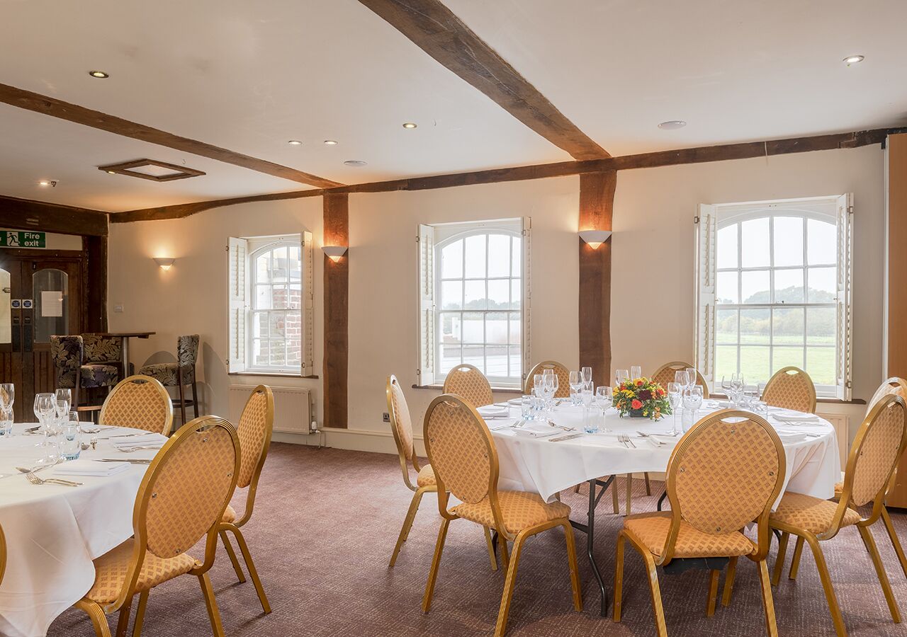 Un espace repas avec des tables rondes disposées pour accueillir six personnes, chacune étant recouverte d’une nappe blanche, entourée de chaises dorées et agrémentée d’un centre de table.