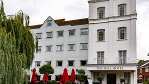 A white building with "The Mill Hotel" sign, a brick bridge, and a duck swimming in a pond. - The Mill Hotel (Sudbury)