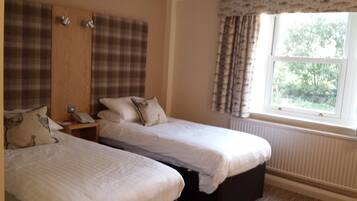 A bedroom with two single beds, a wooden wardrobe, a nightstand with a phone, and a window with curtains.
