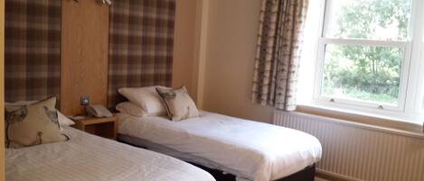 A bedroom with two single beds, a wooden wardrobe, a nightstand with a phone, and a window with curtains.