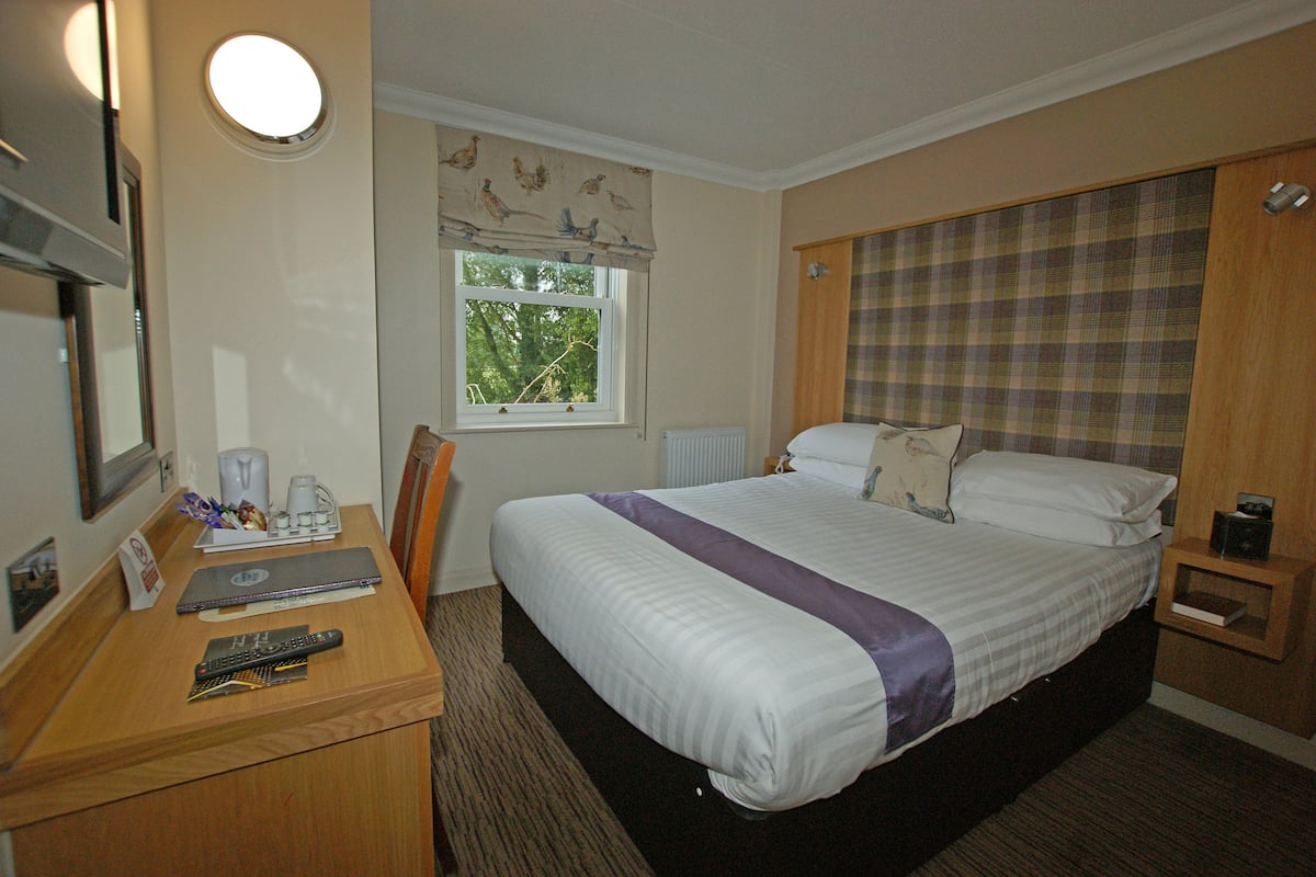 Une chambre d’hôtel comprenant un lit, un bureau avec un ordinateur portable, une chaise, une fenêtre et une table de chevet.