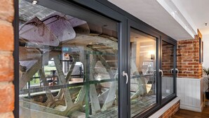 A modern interior with a glass enclosure displaying industrial elements, a brick wall, and a wooden floor. - The Mill Hotel (Sudbury)