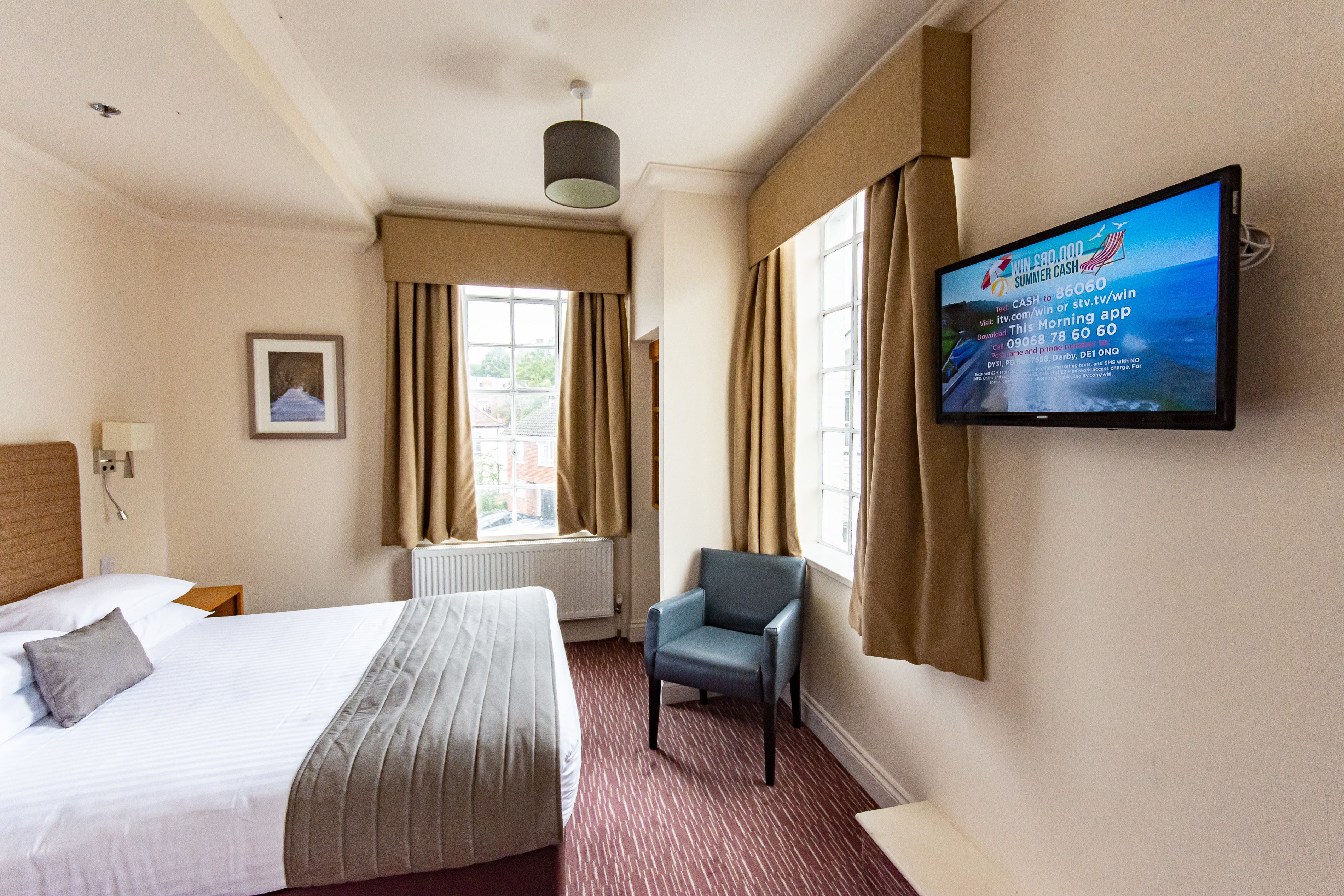Habitación de hotel con dos camas, un televisor, una silla y una ventana con cortinas.