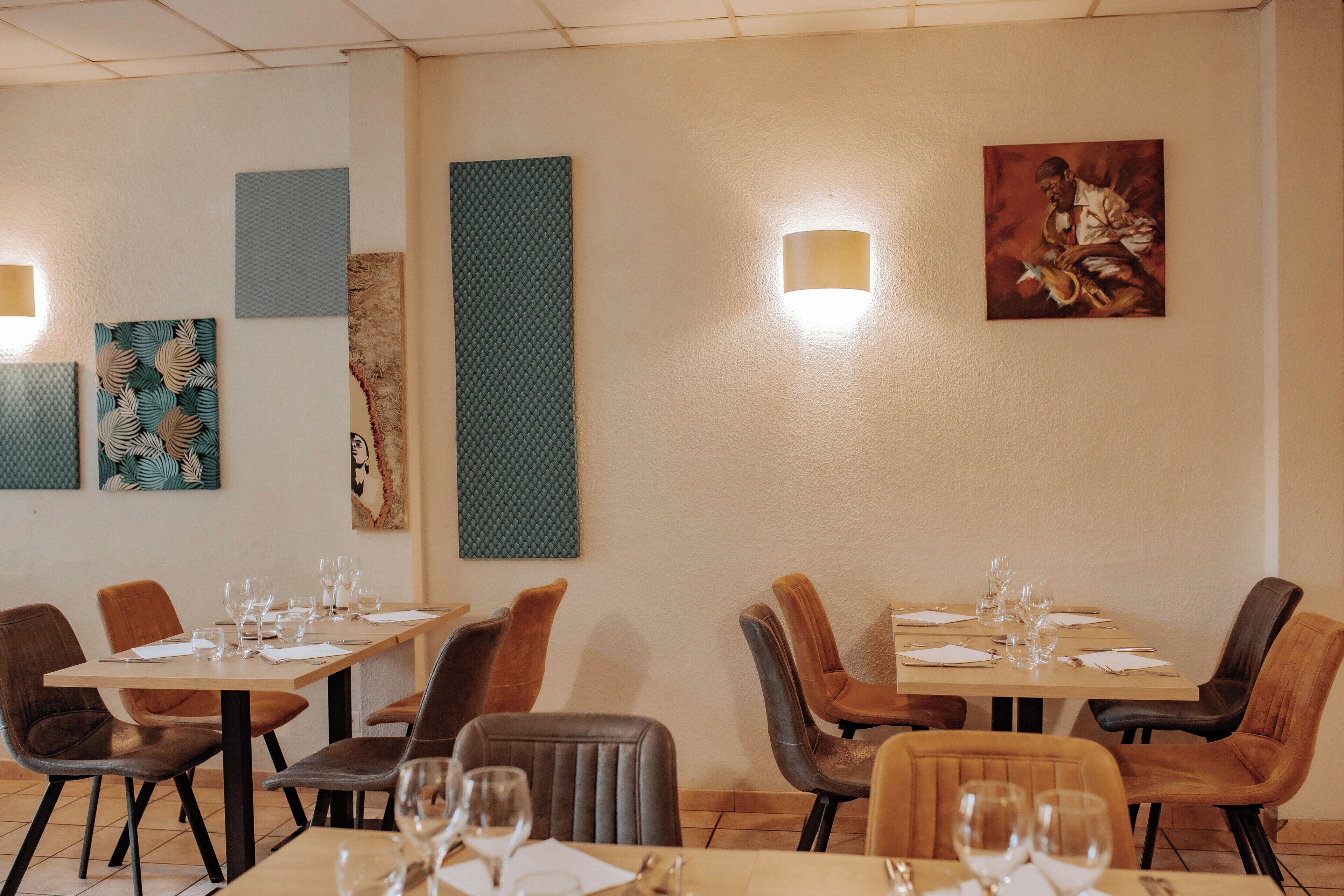 A dining area with tables set for four, each with four chairs. There are wall-mounted light fixtures and artwork on the walls.