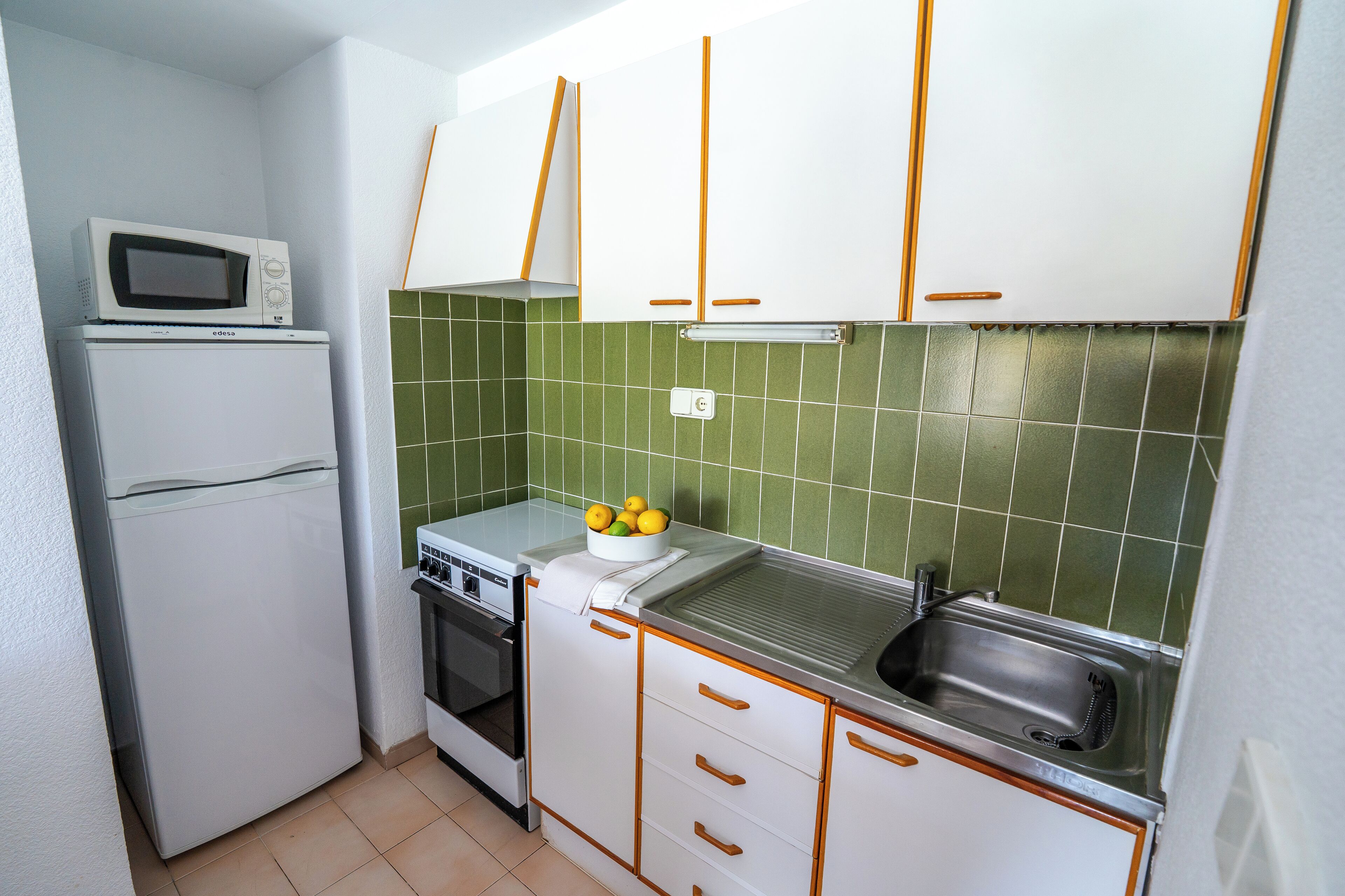 A compact kitchen with white cabinets, a microwave, a stove, and a sink.
