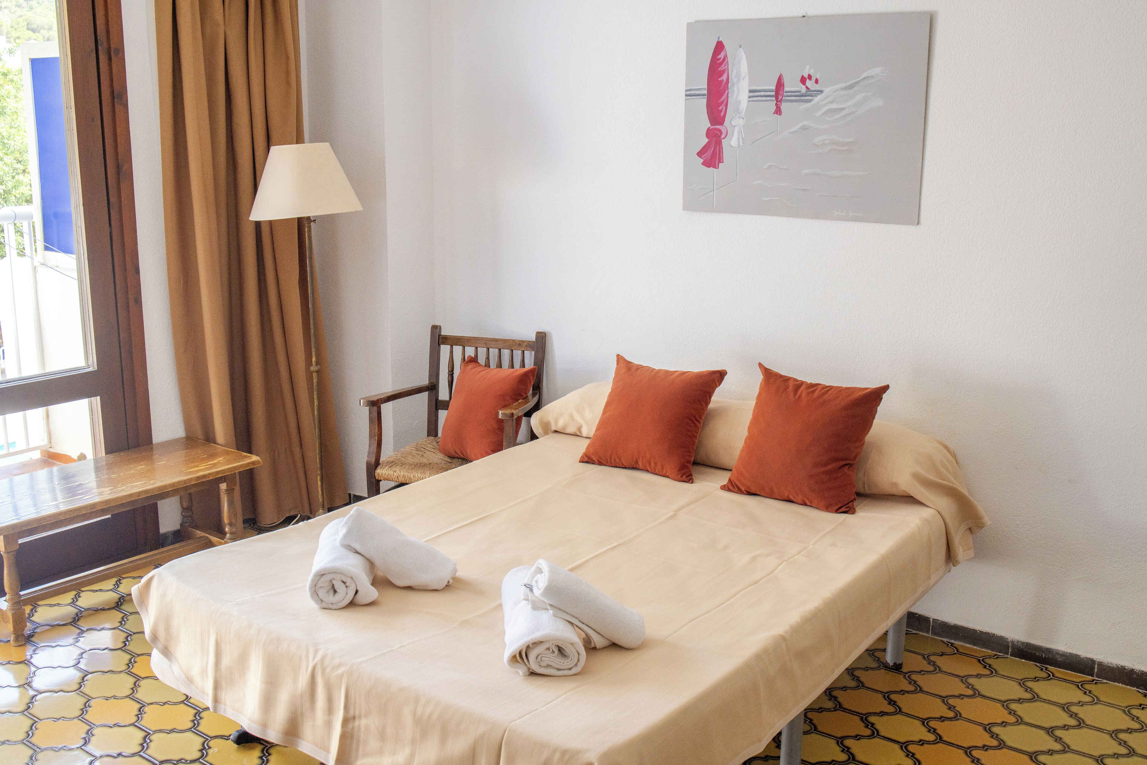 A hotel room with a bed, two pillows, a chair, a table, and a lamp.