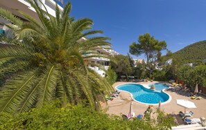A pool area with palm trees, lounge chairs, and a clear blue sky. - Apartamentos Cala LLonga Playa Ibiza (Santa Eulalia del Rio)