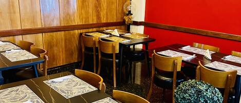 Interior de restaurante con paredes de paneles de madera, varias mesas con manteles individuales y una pantalla de televisión mostrando un programa.