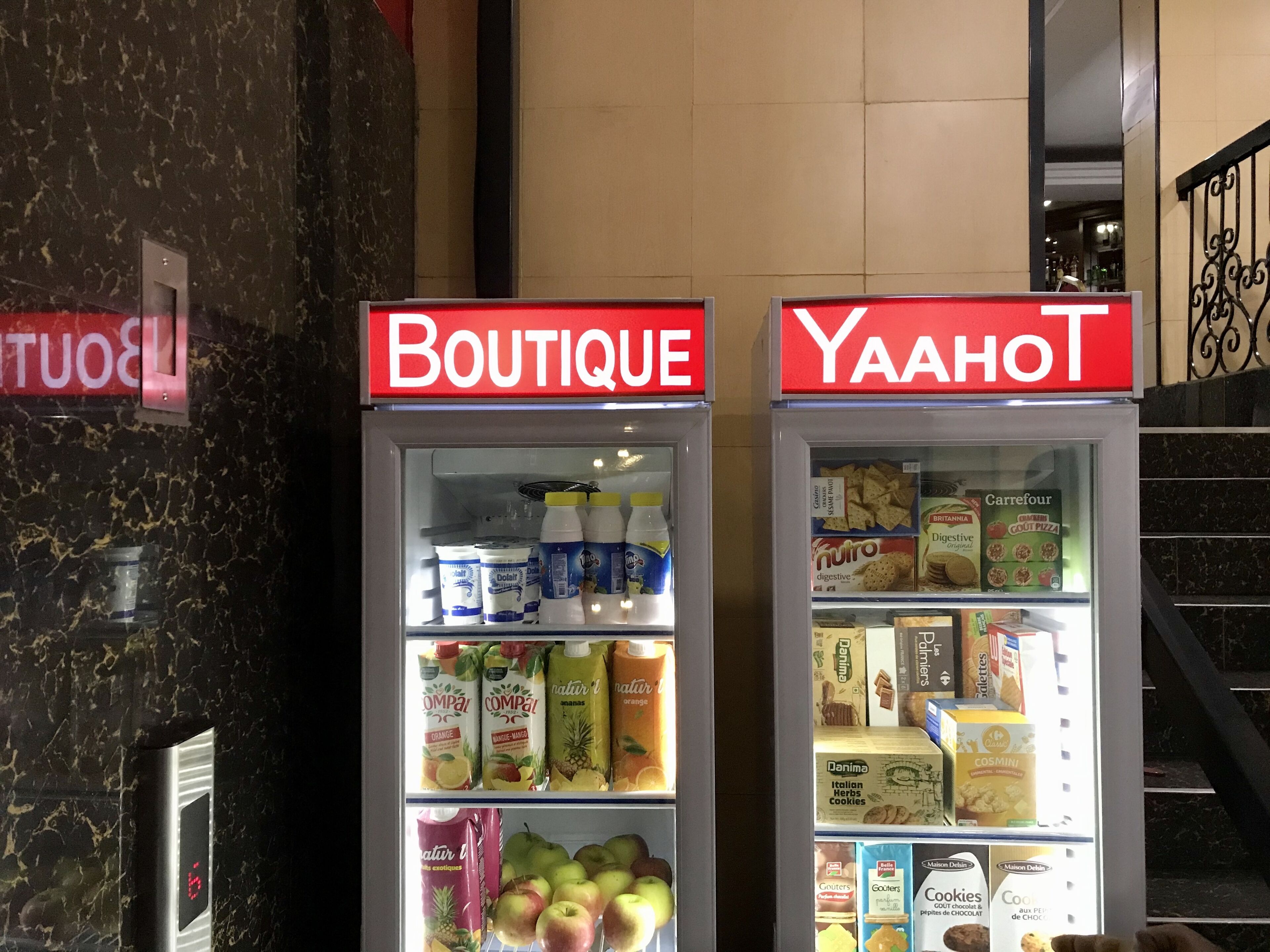 Deux vitrines réfrigérées, portant les inscriptions « BOUTIQUE » et « YAAHOT », contiennent divers produits alimentaires.