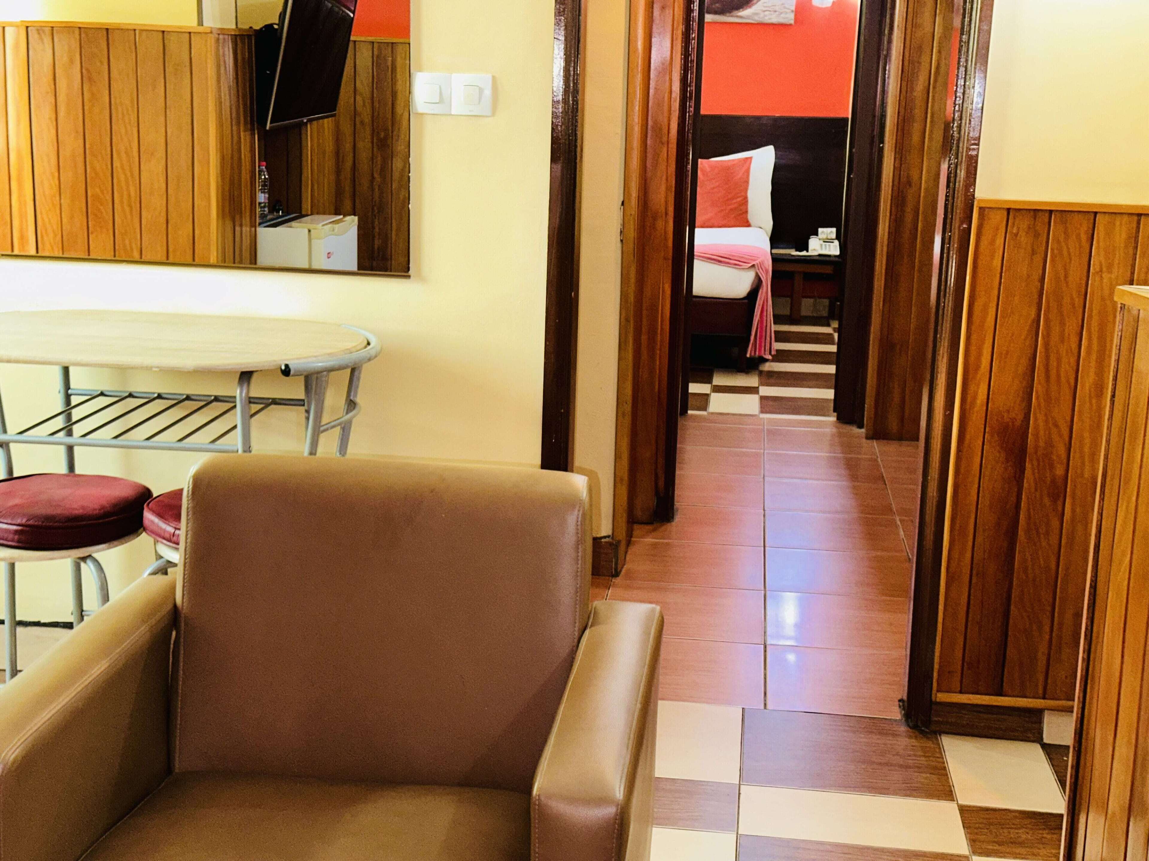 A hotel room with a brown leather chair, a small table with a chair, a wooden cabinet, and a checkered floor.