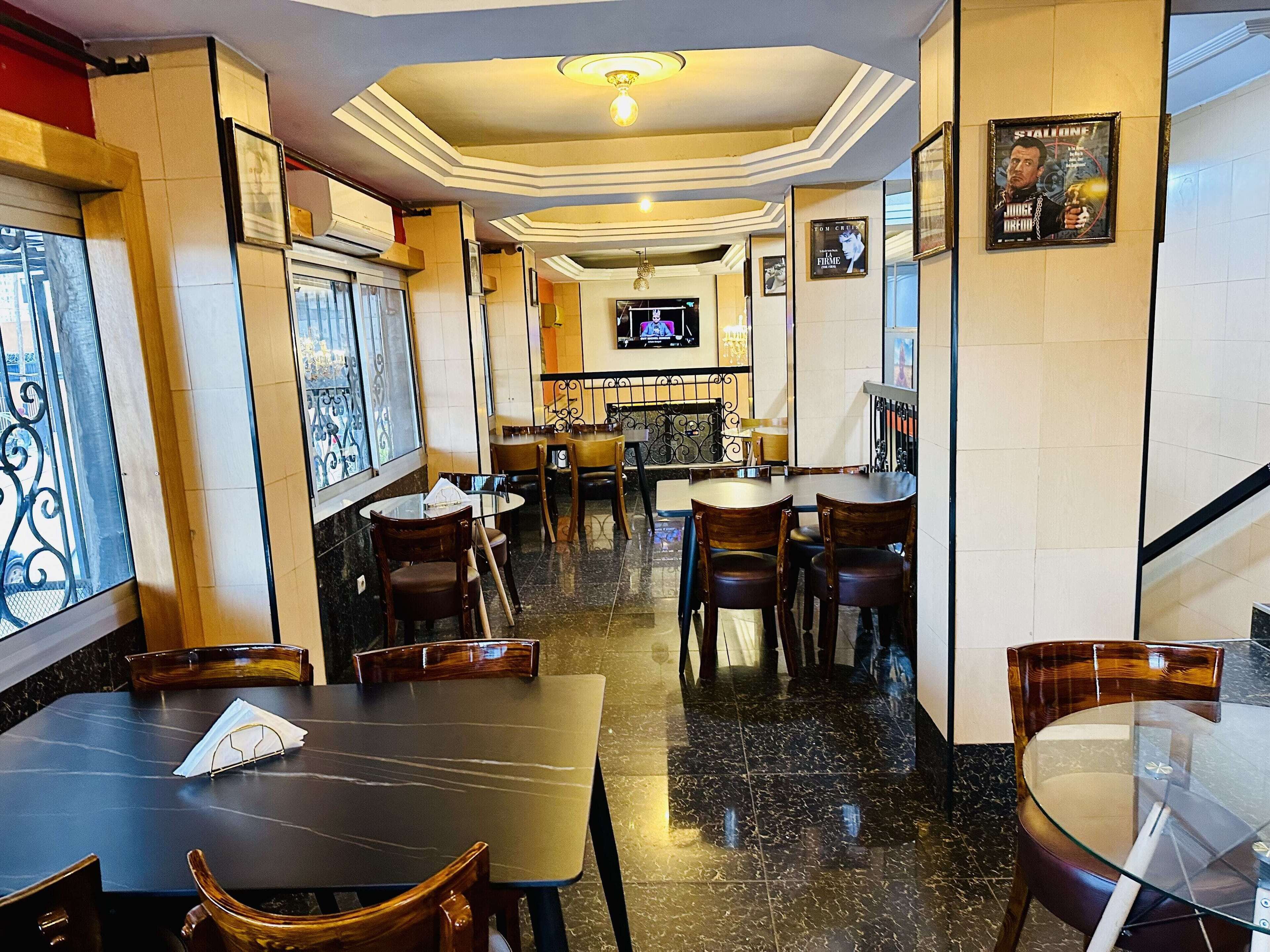 Een restaurant met marmeren vloeren, houten tafels en stoelen, een televisie en inlijstingen aan de muren.