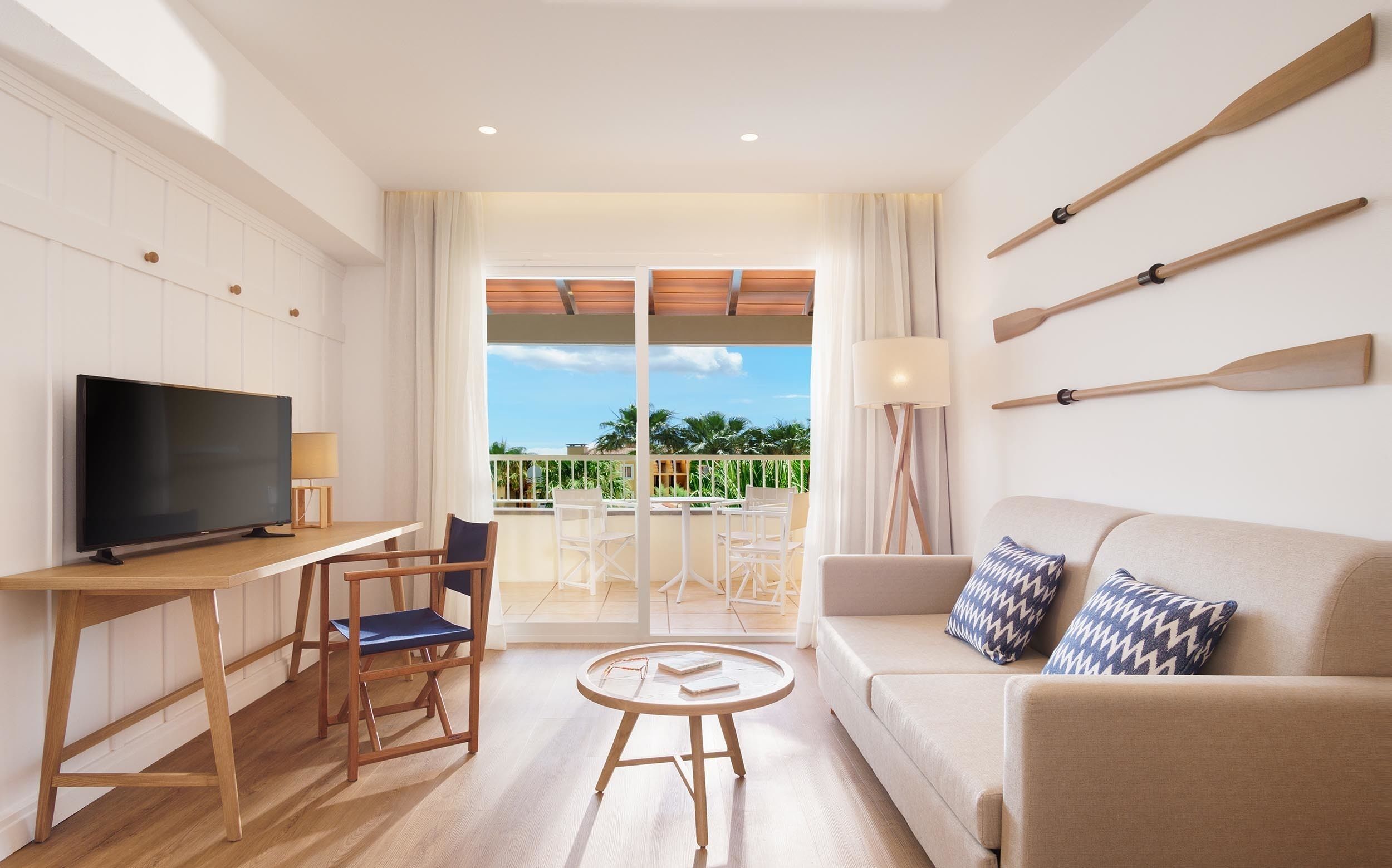 Una sala de estar moderna con un televisor de pantalla plana, muebles de madera, un sofá con cojines estampados y vistas a un balcón con mobiliario exterior.