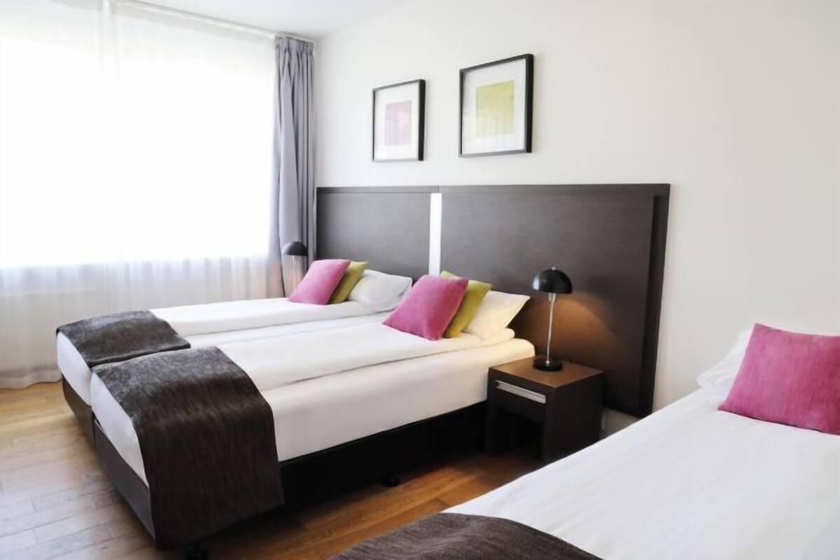 Ein Hotelzimmer mit zwei Betten, einem Nachttisch, einer Lampe und einem Fenster mit Vorhängen.