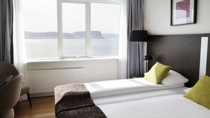 A hotel room with a large window offering a view of the sea, a bed with white bedding and two pillows, a bedside table, and a lamp. - Fosshotel Westfjords (Vesturbyggð)