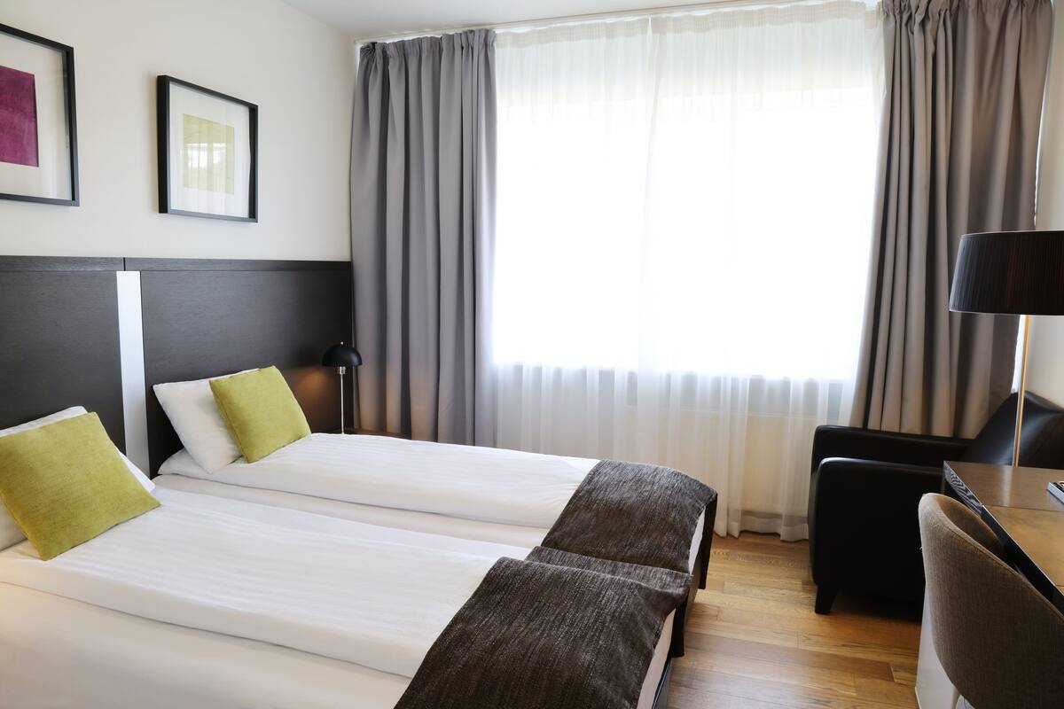 Ein Hotelzimmer mit zwei Betten, einem Schreibtisch, einem Stuhl und einer Lampe.