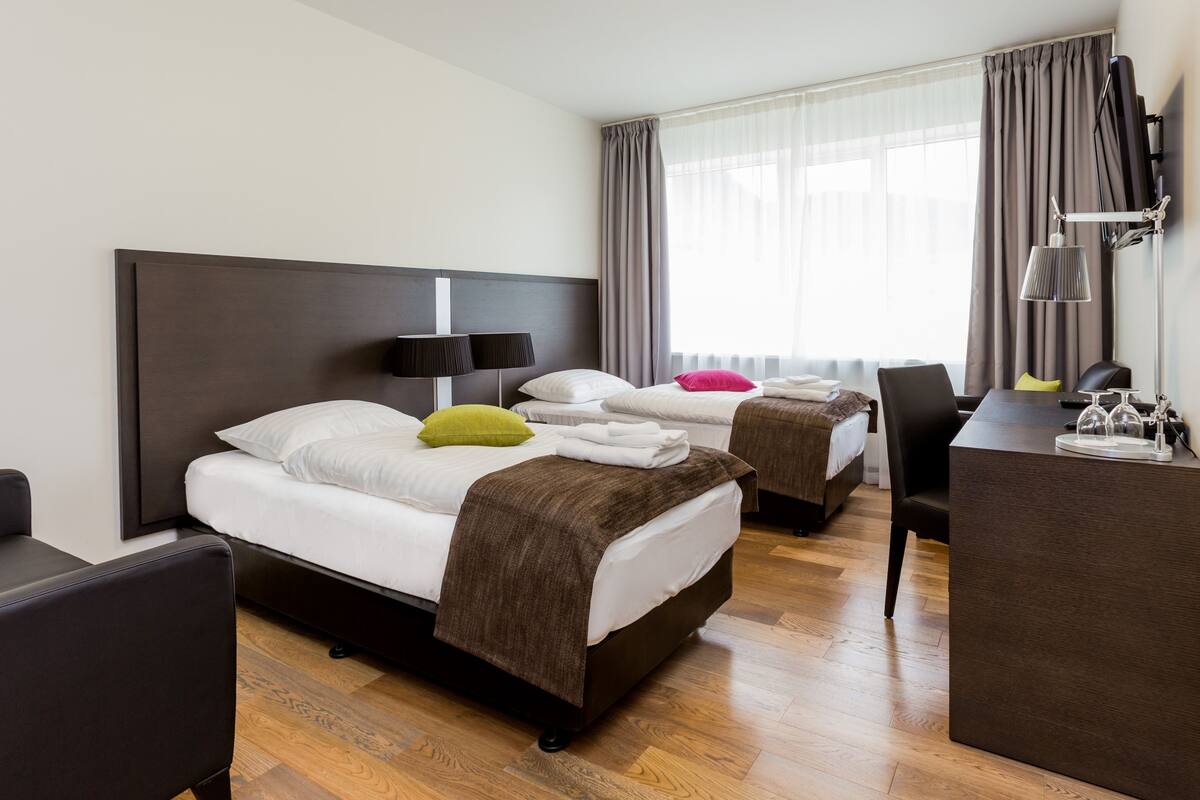 Ein Hotelzimmer mit zwei Betten, einem Schreibtisch, einem Stuhl und einem Fernseher.