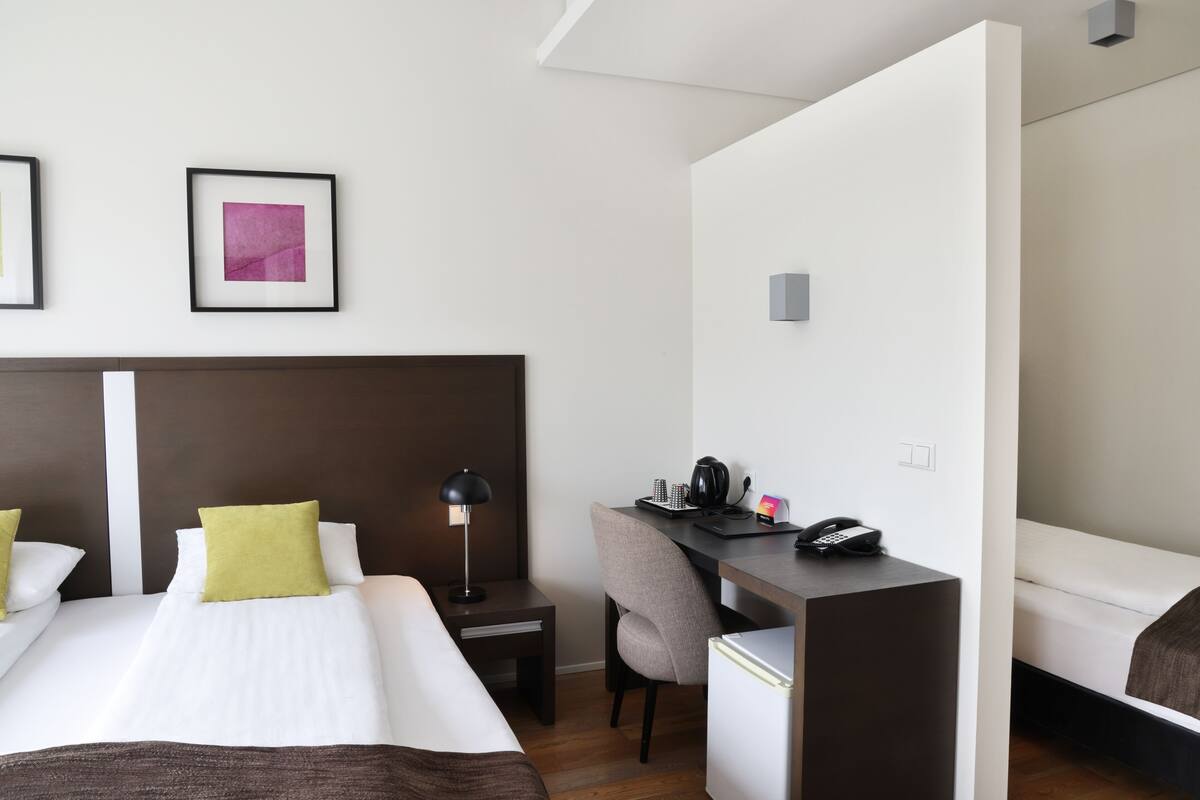 Ein Hotelzimmer mit einem großen Bett, einem Schreibtisch mit Stuhl, einem kleinen Tisch und einem Kühlschrank.