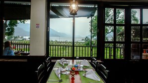 Un comedor con una mesa dispuesta para dos personas, vista a un lago y una montaña al fondo.