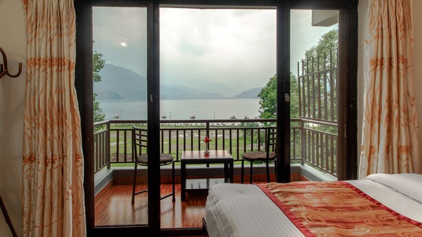 Una habitación con cama, una mesa y una silla, y un balcón con vistas a un lago y montañas.