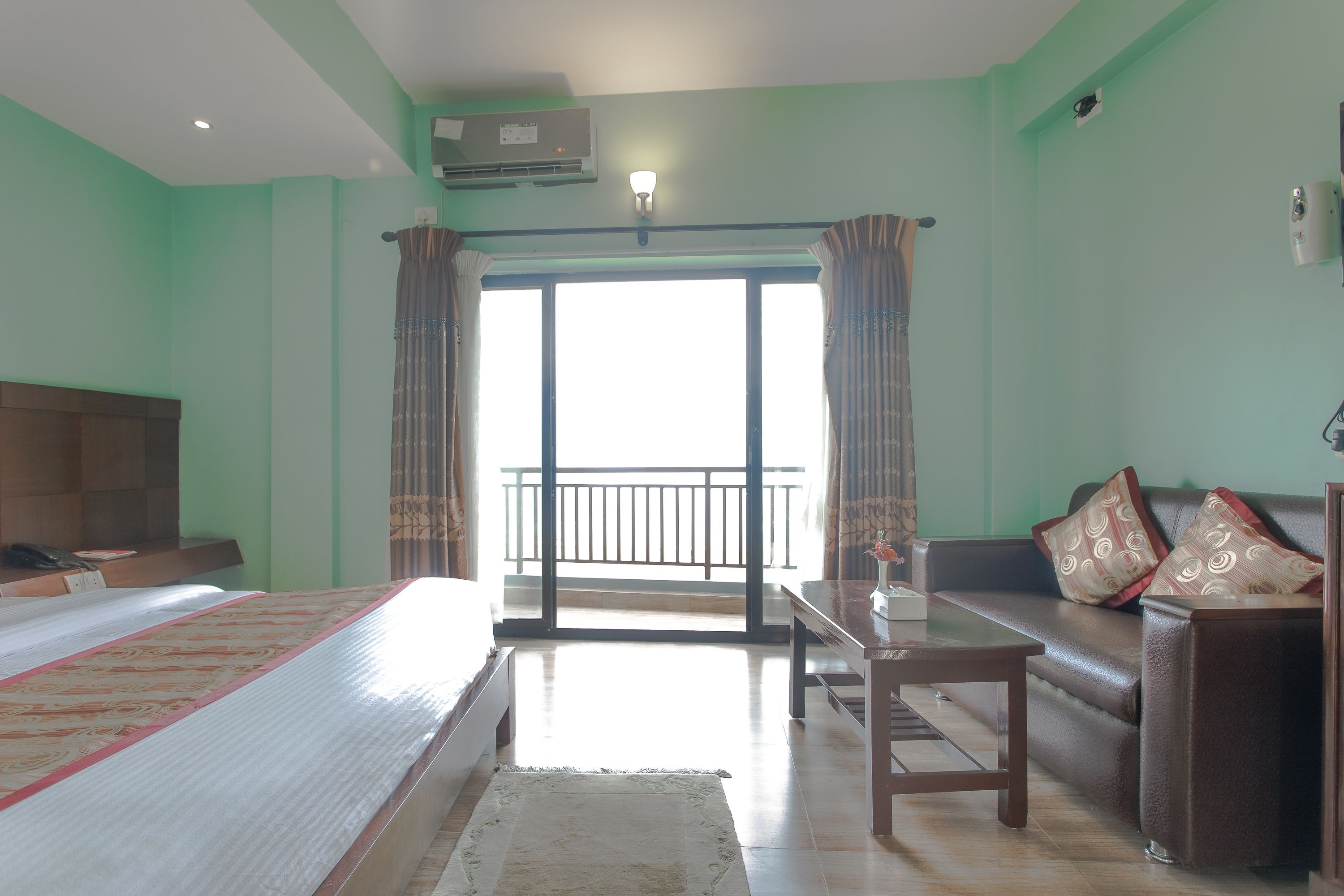 A hotel room with a bed, a sofa, a table, and a balcony with curtains.