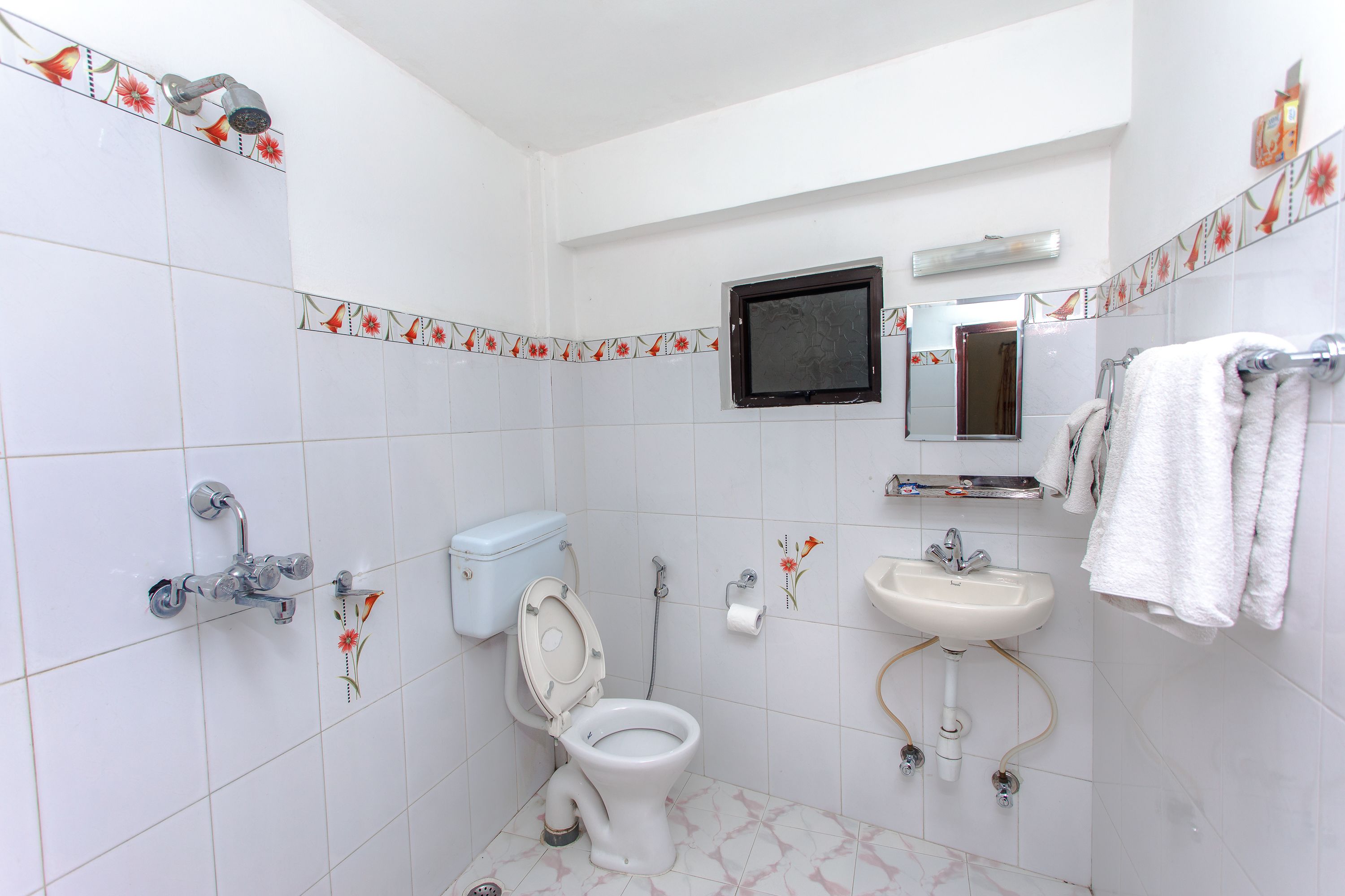 A bathroom with a toilet, sink, shower, and a mirror.