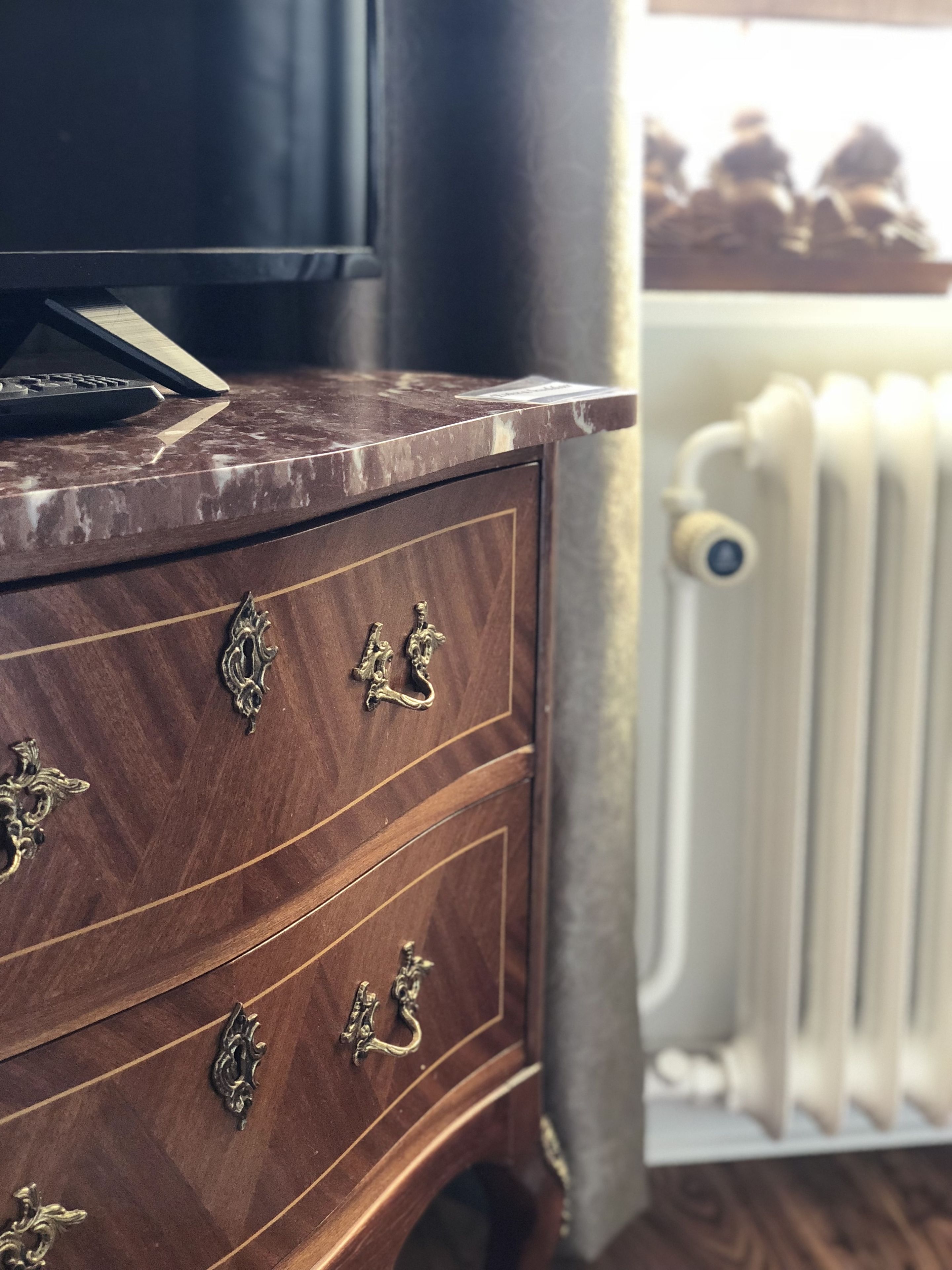 A wooden dresser with ornate metal handles, a remote control on top, and a radiator in the background.