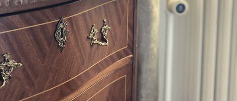 A wooden dresser with ornate metal handles, a remote control on top, and a radiator in the background.