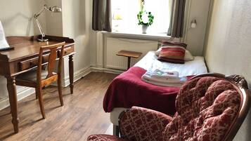 Une chambre avec un bureau en bois, une chaise, un lit recouvert d’une couverture rouge et une fenêtre avec des rideaux.