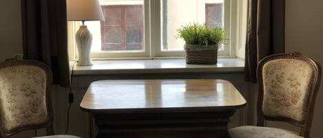 A room with a table and two chairs, a window with curtains, a lamp, and a potted plant on the windowsill.