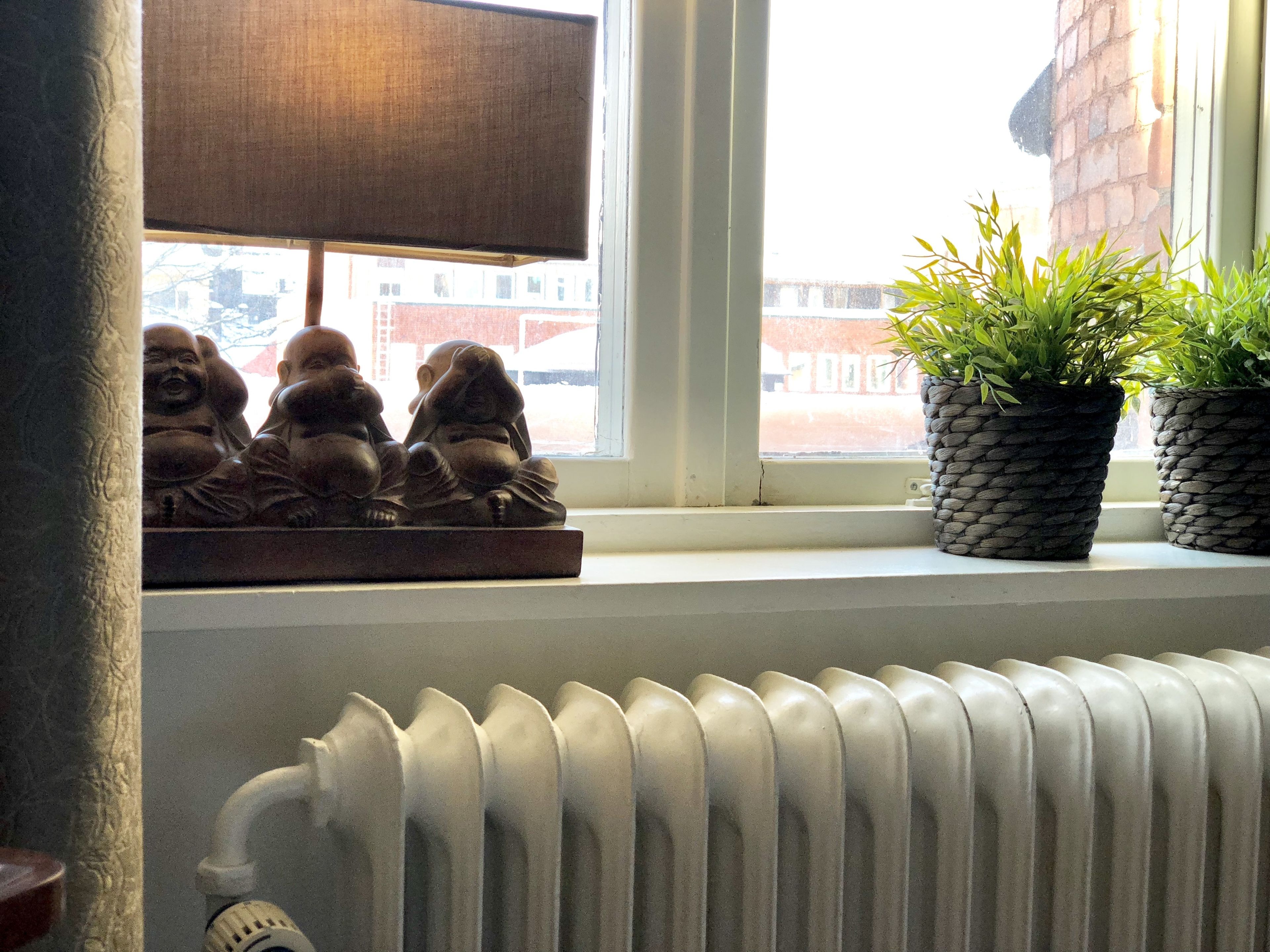 A window with a radiator below and a Buddha statue on the sill.