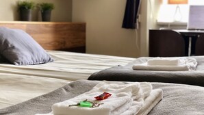 Habitación de hotel con cama, televisión montada en la pared, escritorio con lámpara y ventana con cortinas.
