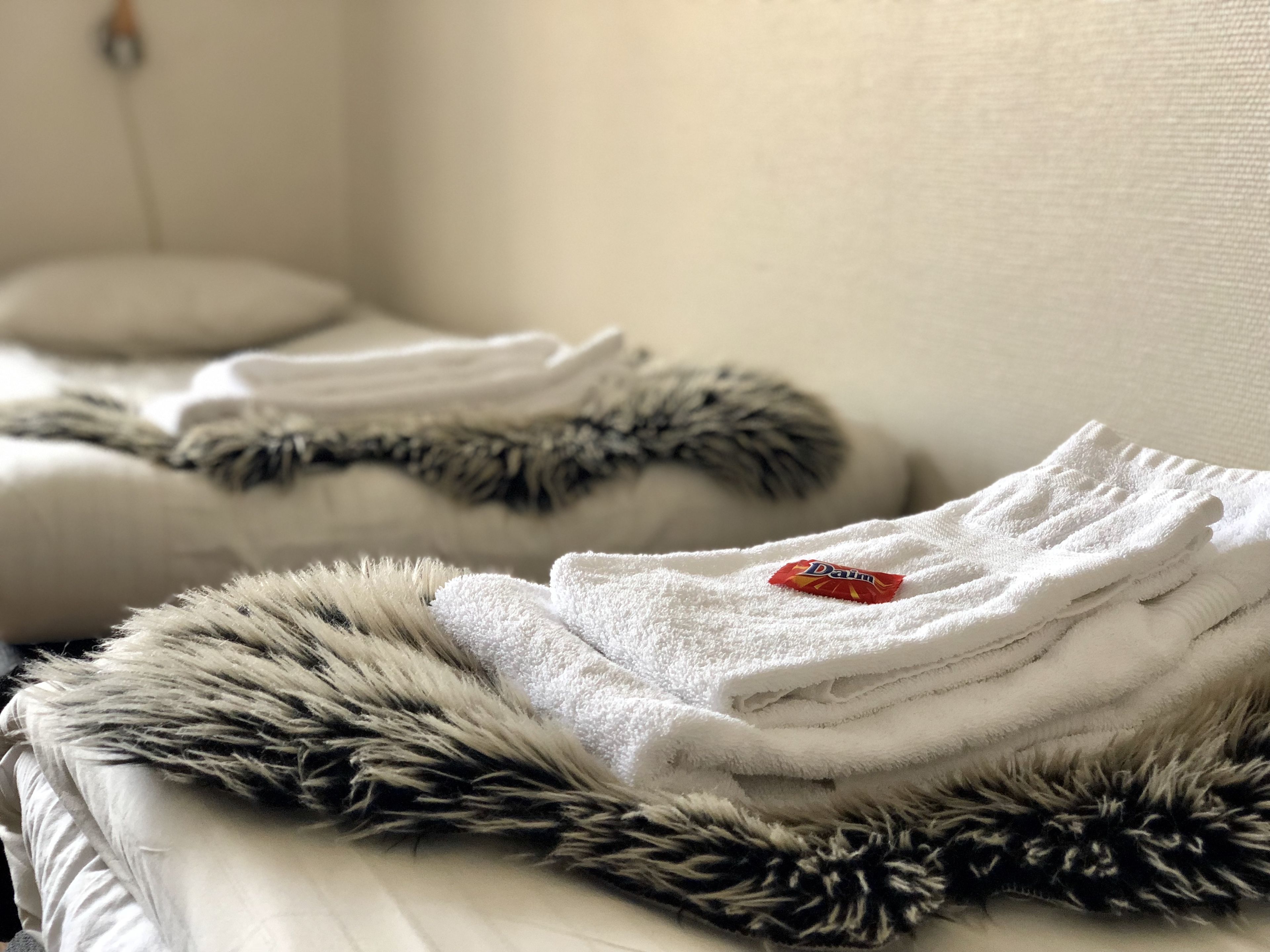 Ein ordentlich gemachtes Bett mit einer flauschigen Decke in Dunkel- und Hellgrau sowie einem weißen Handtuch mit rotem Etikett.