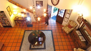 A hotel lobby with a tiled floor, a chandelier, a round table with a vase, a sofa, and a wooden cabinet with papers.