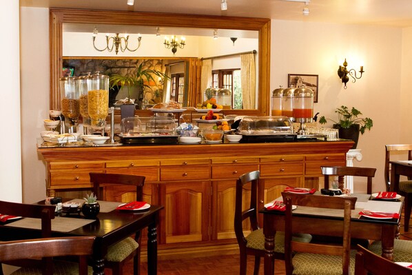 Un comedor de hotel con muebles de madera, una barra de buffet y un espejo grande que refleja el salón.