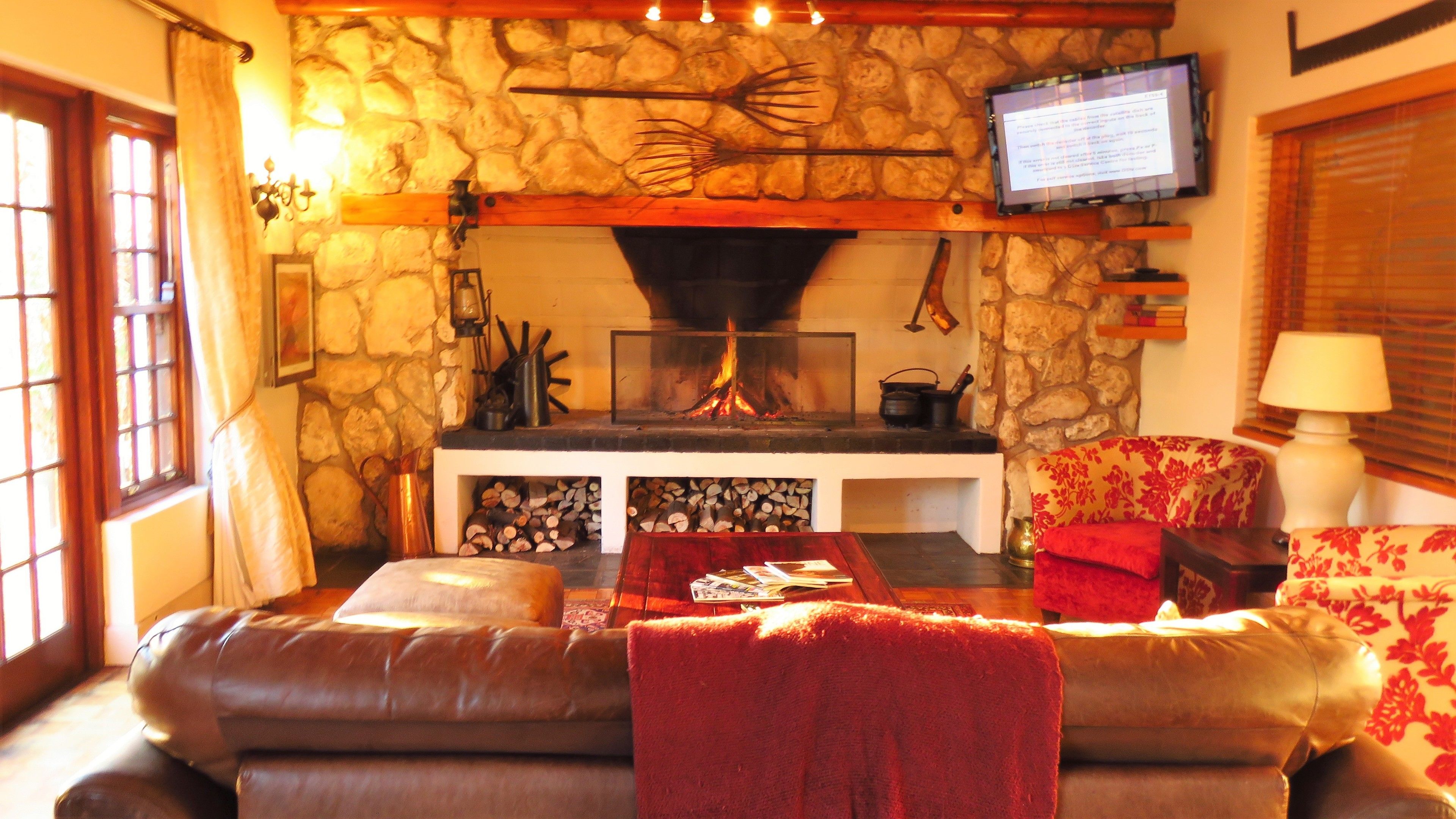 A cozy living room with a stone fireplace, a television mounted above it, and a comfortable sofa with a red throw blanket.