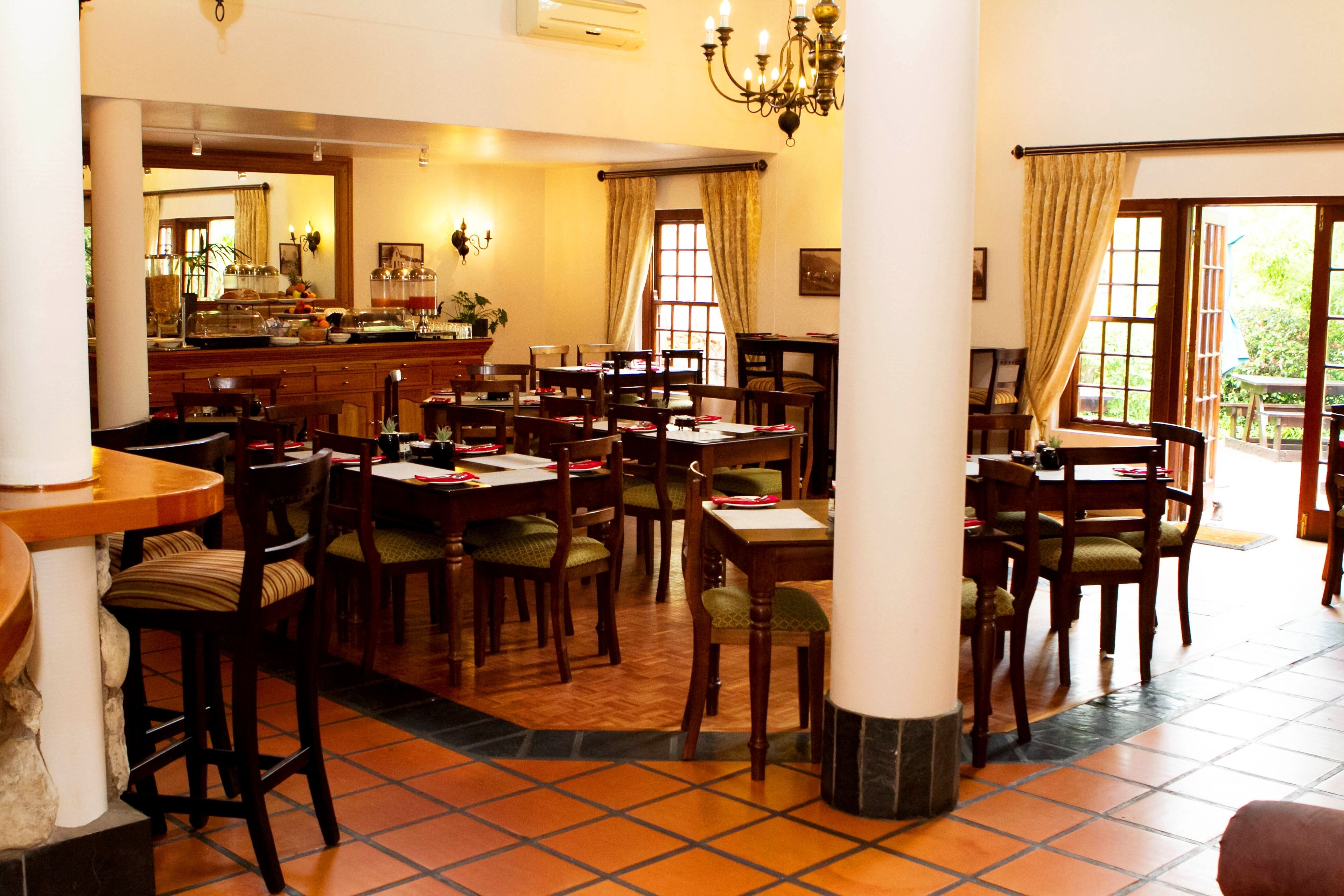 A dining area with multiple tables and chairs, a bar area with various items, and large windows with curtains.