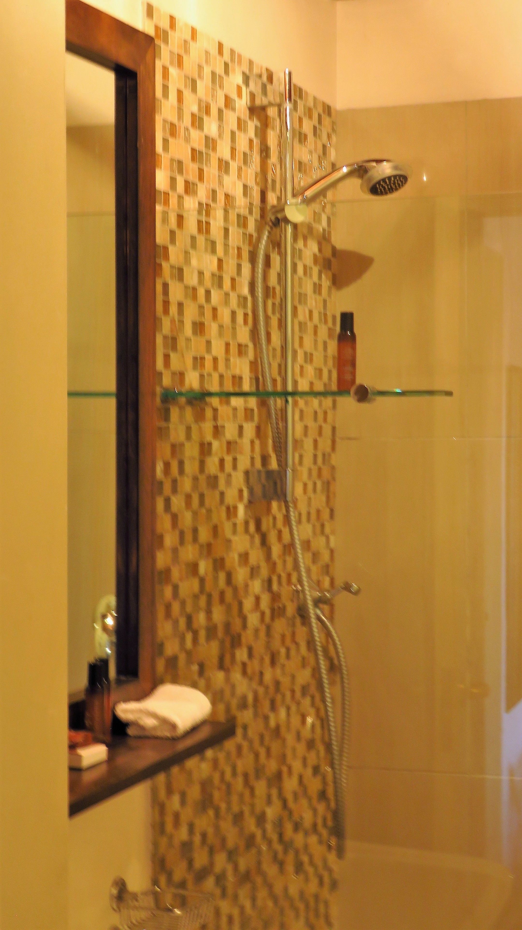 Ein Badezimmer mit Dusche, einer Glasablage für Pflegeprodukte und einem Spiegel.