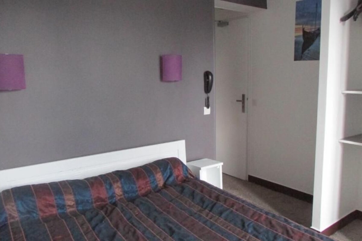 A bedroom with a bed, a wardrobe, a bedside table, and a wall-mounted telephone.
