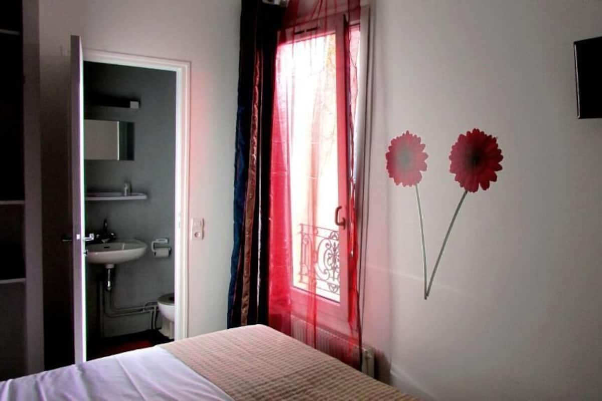 A bedroom with a bed, a bathroom with a sink, and a TV mounted on the wall.